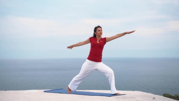 Young slim female doing yoga warrior pose near the sea — Stock Video
