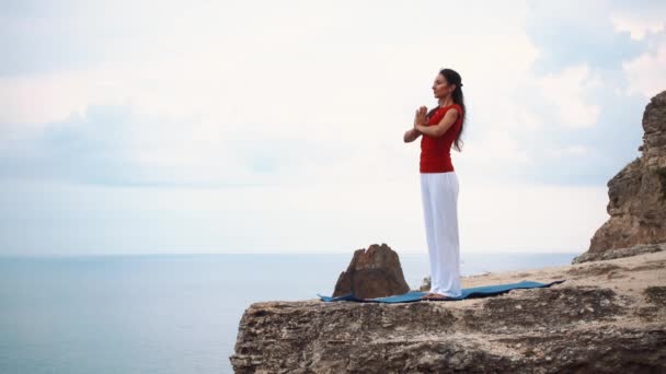 Mujer de pie y meditando en un acantilado sobre el océano. Yoga en el acantilado . — Vídeos de Stock