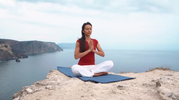 Fille assise sur le rocher par la mer, méditant dans la pose de yoga lotus, se concentrant, esprit relaxant, âme et corps . — Video