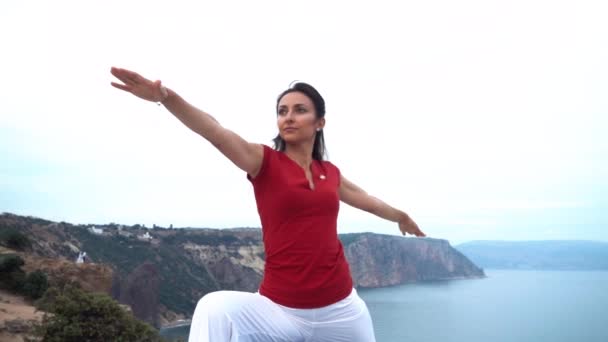 Joven hembra delgada haciendo yoga guerrero pose cerca del mar cámara lenta — Vídeos de Stock