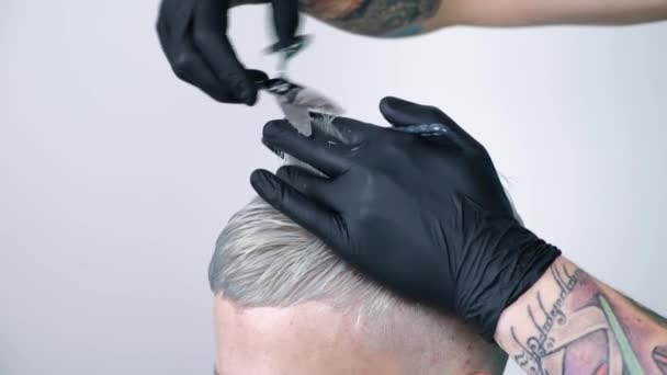 Hombre que se corta el pelo con tijeras de pelo rubio sobre un fondo blanco — Vídeos de Stock