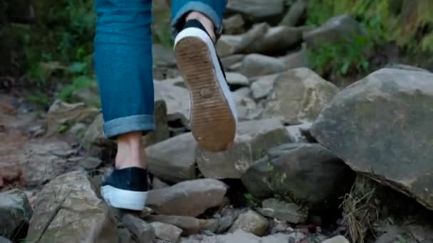 Bir sürü taş bir dağ yolu üzerinde tek başına yürüyen bir kadın kot pantolon ve crossover, bacaklar — Stok video