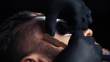 Yakın çekim yakışıklı bir adamın sakalını tıraş bir Kuaför profesyonel kuaför müşteri mesleği tıraş jilet kullanarak alma.