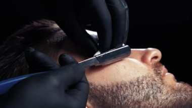 Yakın çekim yakışıklı bir adamın sakalını tıraş bir Kuaför profesyonel kuaför müşteri mesleği tıraş jilet kullanarak alma.