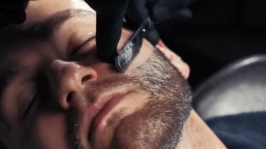 Yakın çekim yakışıklı bir adamın sakalını tıraş bir Kuaför profesyonel kuaför müşteri mesleği tıraş jilet kullanarak alma.