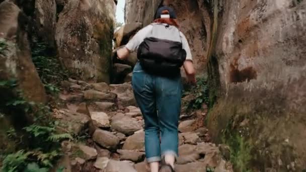 Trekking in montagna. Vista posteriore della schiena di una giovane donna di hockey che cammina lungo la strada con uno zaino attraverso il canyon di montagna — Video Stock