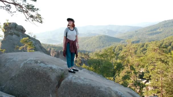Wanderer mit Rucksack auf dem Gipfel eines Berges mit Sonnenstrahlen. junge Frau gesunde aktive Lebensweise. Abenteuer in der Natur. 4k — Stockvideo