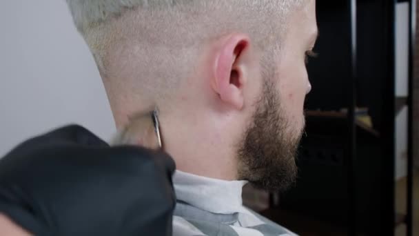 Het maken van kapsel. Young bebaarde man krijgen kapsel door barber zittend in de stoel bij barbershop — Stockvideo