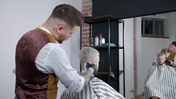 Tattoed barbiere rende taglio di capelli per il cliente presso il negozio di barbiere utilizzando tagliacapelli, taglio di capelli mans e rasatura presso il parrucchiere, barbiere e salone da barba . — Video Stock