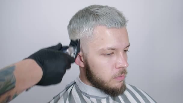 Het maken van kapsel. Young bebaarde man krijgen kapsel door barber zittend in de stoel bij barbershop. — Stockvideo