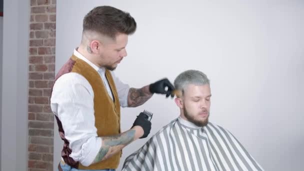 Faire une coupe de cheveux. Jeune homme barbu se faire couper les cheveux par barbier alors qu'il était assis sur une chaise au salon de coiffure . — Video