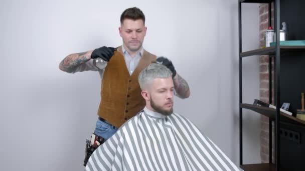 Професійний баба, що працює зачіскою, розчісує її водою. чоловічий клієнт з світлим волоссям . — стокове відео