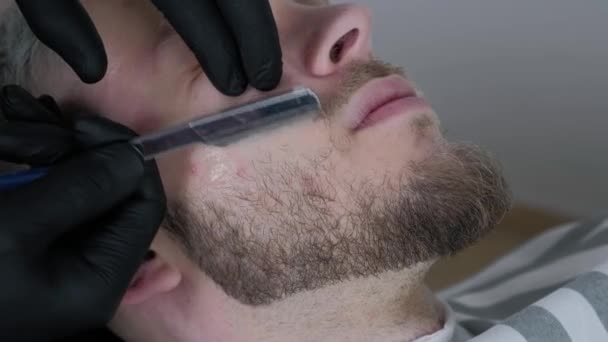 Beard cut with straight razor shave. Close up of shaving beard in barber shop. Male beard style. Barber shaving hipster man face — Stock Video