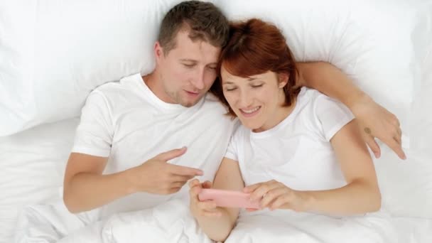 Ehepaare liegen im Bett und schauen auf Smartphones - kommunizieren in sozialen Netzwerken und schreiben vor dem Zubettgehen Nachrichten im Bett liegend. — Stockvideo