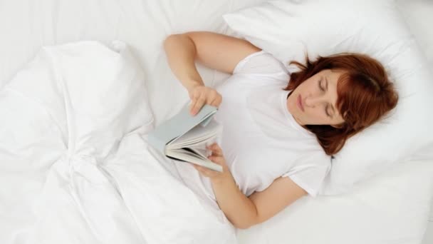 Счастливая девушка читает книгу в белой кровати. вид сверху — стоковое видео