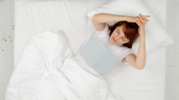 Menina feliz lendo um livro em uma cama branca. vista superior — Vídeo de Stock