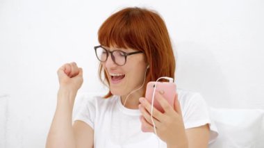 dikey bir kızın telefon ile bir akıllı telefon gülümseyen sizin en sevdiğiniz melodi bulmak, beyaz bir arka plan üzerinde izole kulaklık, dinlemek.