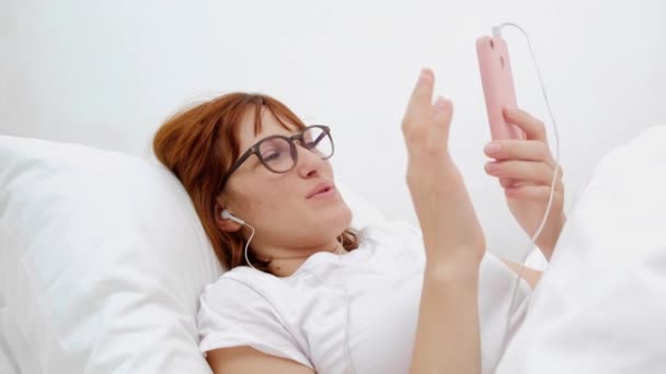 Patienten talar i mobiltelefon i sängen. Ung attraktiv kvinna i sjukhussäng. Ansluten världen och mobila office-konceptet. — Stockvideo