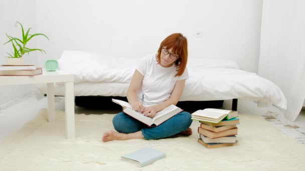 Mulher bonita sentada em seu chão da sala de estar improvisando usando pilhas altas de livros — Vídeo de Stock