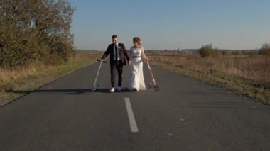 Ellerinde bir scooter ile güzel yeni evliler Altın Sonbahar yolda yürüyor