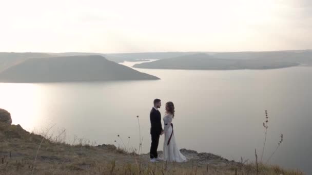 En man och en kvinna står på kanten av en klippa nära havet, håret utvecklar i vinden. Vita kläder. — Stockvideo