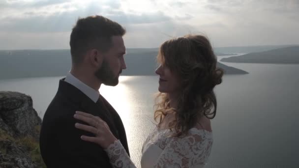 A man and a woman are standing on the edge of the cliff near the ocean, the hair is developing in the wind. White clothes. — Stock Video