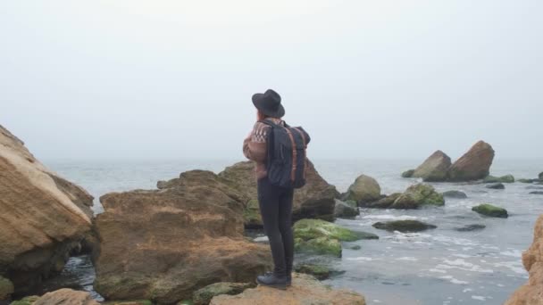 Young girl tourist looks at the ocean. in hat and backpack — 비디오