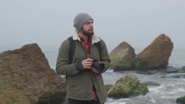 Fotógrafo al aire libre con barba capturando un mar tormentoso — Vídeo de stock
