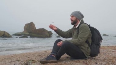 Young bearded man throws stones at the water in the evening.