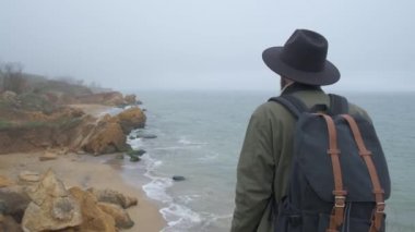 Bir şapka ve ceket bir sahil cep telefonu kullanarak güzel doğal sahnelerin fotoğraflarını çeken şık bir adam Backview. Vahşi soğuk gün
