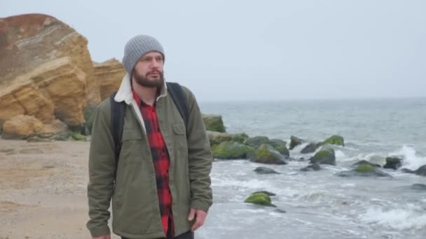 Pensive man går längs havet. Han ser fram emot och i kameran, kallt fall väder — Stockvideo