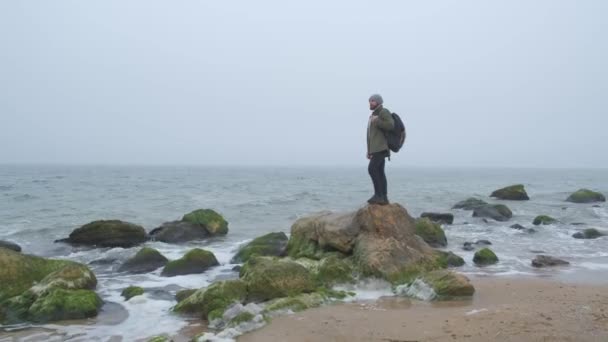 One lone tourist in the wilderness with stone mountains and coast. Coast and good feelings, the emotional concept of life. Hipster thinking and looking at the horizon — Stock Video