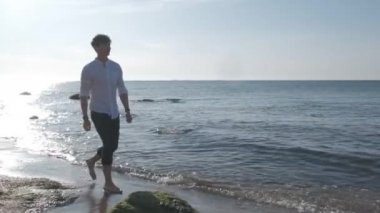 Gün doğumunda deniz sahilinde yürüyen adam