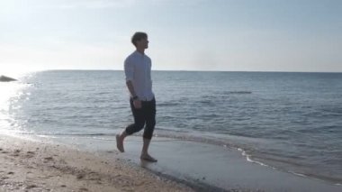 Gün doğumunda deniz sahilinde yürüyen adam