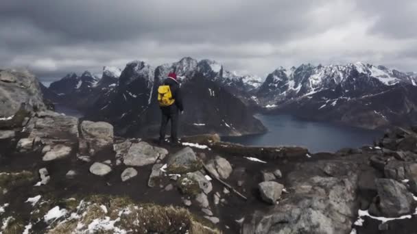 Letecká záběry mužského hikera na vrcholku hory s výhledem na nádhernou scenérii Lofoten Islands v malebném souostroví, Norsko, — Stock video