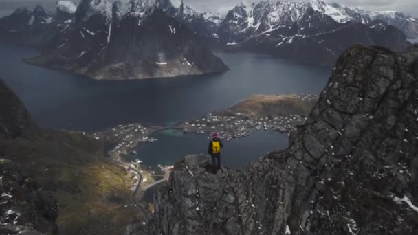 Luftaufnahmen eines männlichen Wanderers auf einem Berggipfel mit Blick auf die wunderschöne Landschaft der Lofoten-Inseln in landschaftlich reizvoller, norwegischer Inselgruppe, — Stockvideo