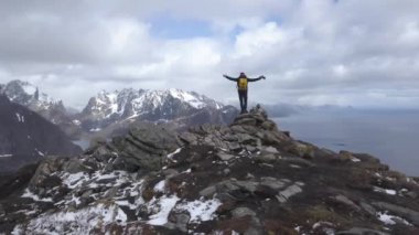 Turist Lofoten içinde uçurumun tırmanıyor. Adam, ellerini zaflerle yükseltir. Macera ve seyahat konsepti. Hava