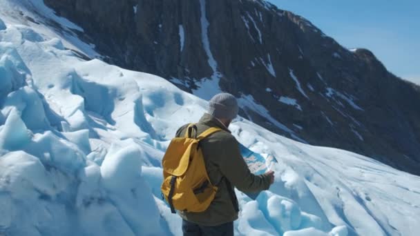 Бородатый мужчина с желтым рюкзаком и туристической картой в руках, на фоне зимнего пейзажа — стоковое видео