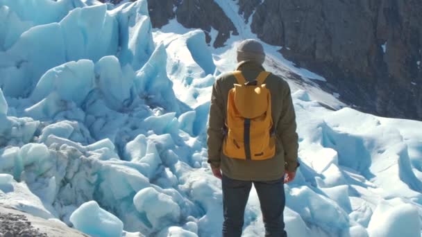 Un turista con una mochila amarilla mira el glaciar Svartisen en Noruega . — Vídeos de Stock