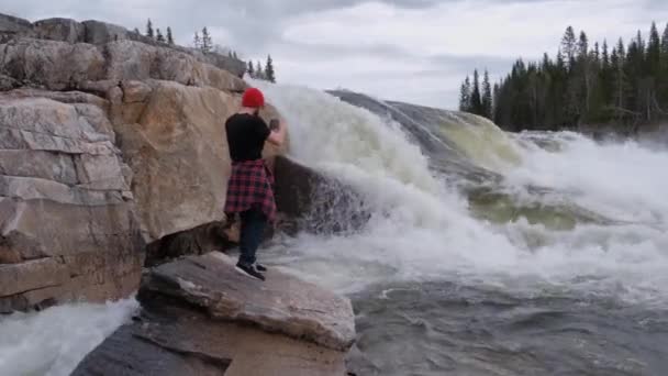 Турист стоит под водопадом, делает фотографии, как вода течет — стоковое видео