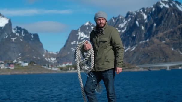 Brutaler Mann mit einem Seil auf der Schulter vor dem Hintergrund der Berge und des blauen Himmels — Stockvideo