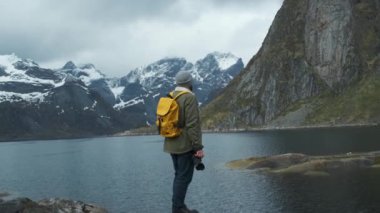 Hiker karlı dağ zirveleri görünümü zevk. Sarı sırt çantası ile erkek otostopçu düşük açı arka görünümü ve karlı dağ zirveleri görünümü zevk