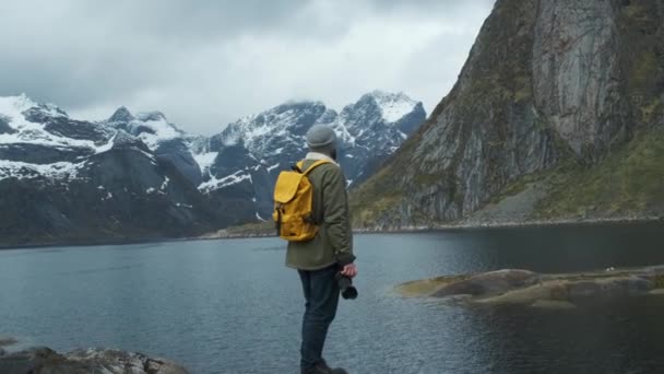 Senderista disfrutando de la vista de los picos nevados de montaña. Vista trasera de ángulo bajo del excursionista masculino con mochila amarilla y disfrutando de la vista de los picos de montaña nevados — Vídeo de stock