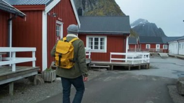 Erkek turist Reine, Lofoten, Norveç köyü aracılığıyla yürür. Mavi gökyüzü, tipik Rorbu evleri ile. İnanılmaz manzara bakıyor adam