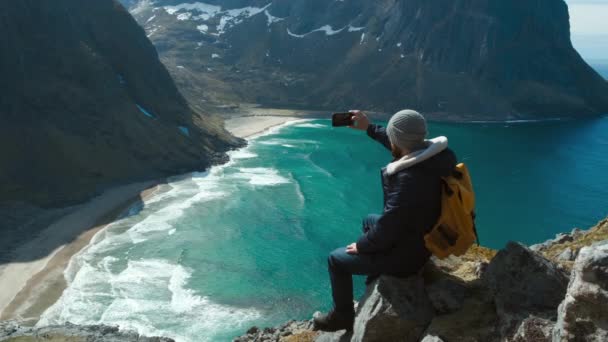 Hipster fotografare valle con smartphone indossare zaino fotografare paesaggio panoramico natura viaggio avventura Norvegia Kvalvika spiaggia . — Video Stock