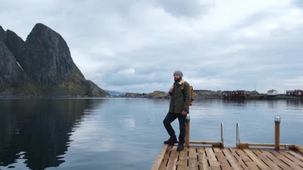 Turista masculino de pie en un muelle de madera y mirando al hermoso paisaje. Increíble mar, superficie de agua tranquila. Altas montañas limpias cielo azul . — Vídeos de Stock