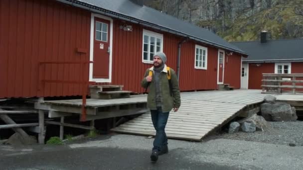 Ο αρσενικός τουριστικός περπατάει με το χωριό Ρεν, Λοφότεν, Νορβηγία. Μπλε ουρανός, με τα τυπικά σπίτια των ρομμπού. Ο άνθρωπος που κοιτάζει το εκπληκτικό τοπίο — Αρχείο Βίντεο