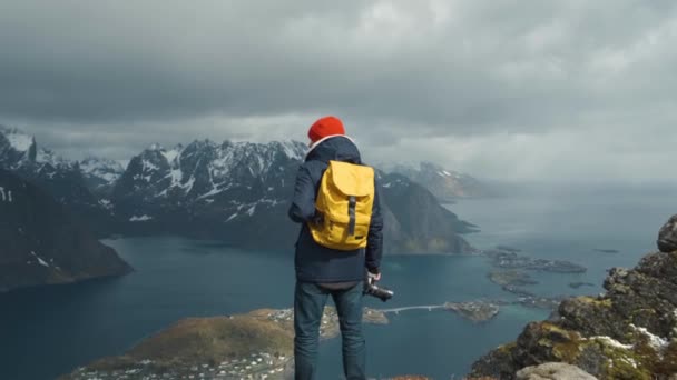 Fotós férfi egy sárga hátizsák, áll a tetején a hegyvidéki természet. kalandtúra koncepció. Norvégia Lofoten Reine — Stock videók