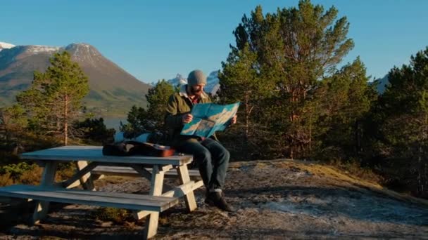 Νέος βίαιος άνθρωπος που κοιτάζει ένα χάρτη σε ένα δάσος το ηλιοβασίλεμα. Δάσος της Νορβηγίας. Ξύλινο τραπέζι για χαλάρωση. — Αρχείο Βίντεο