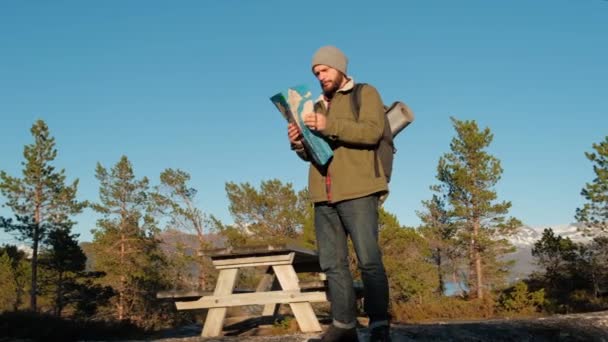 Jonge brutale man op zoek naar een kaart in een bos bij zonsondergang. Het bos van Noorwegen. Houten tafel voor ontspanning. — Stockvideo